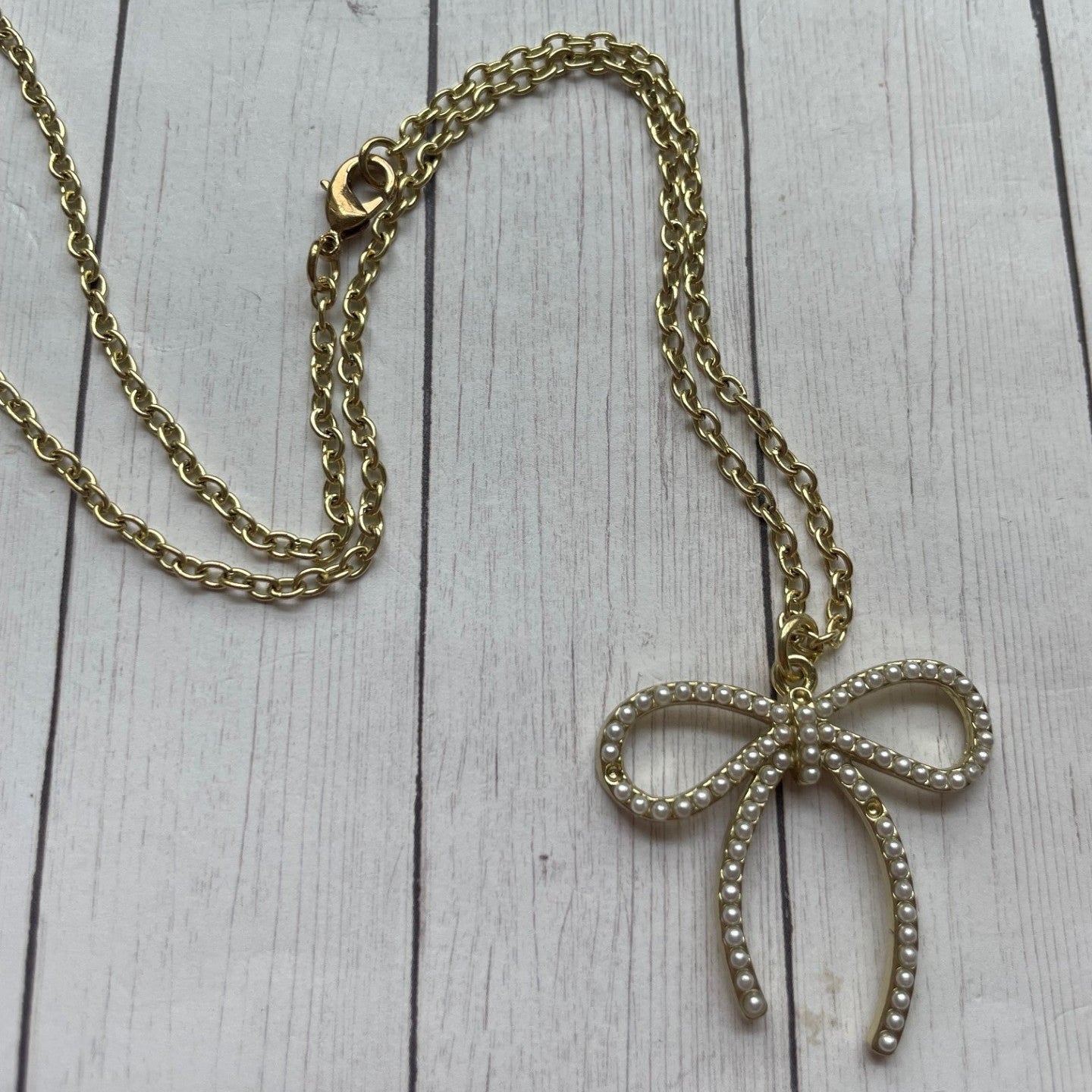 Gold chain necklace with a bow-shaped pendant on a wooden surface