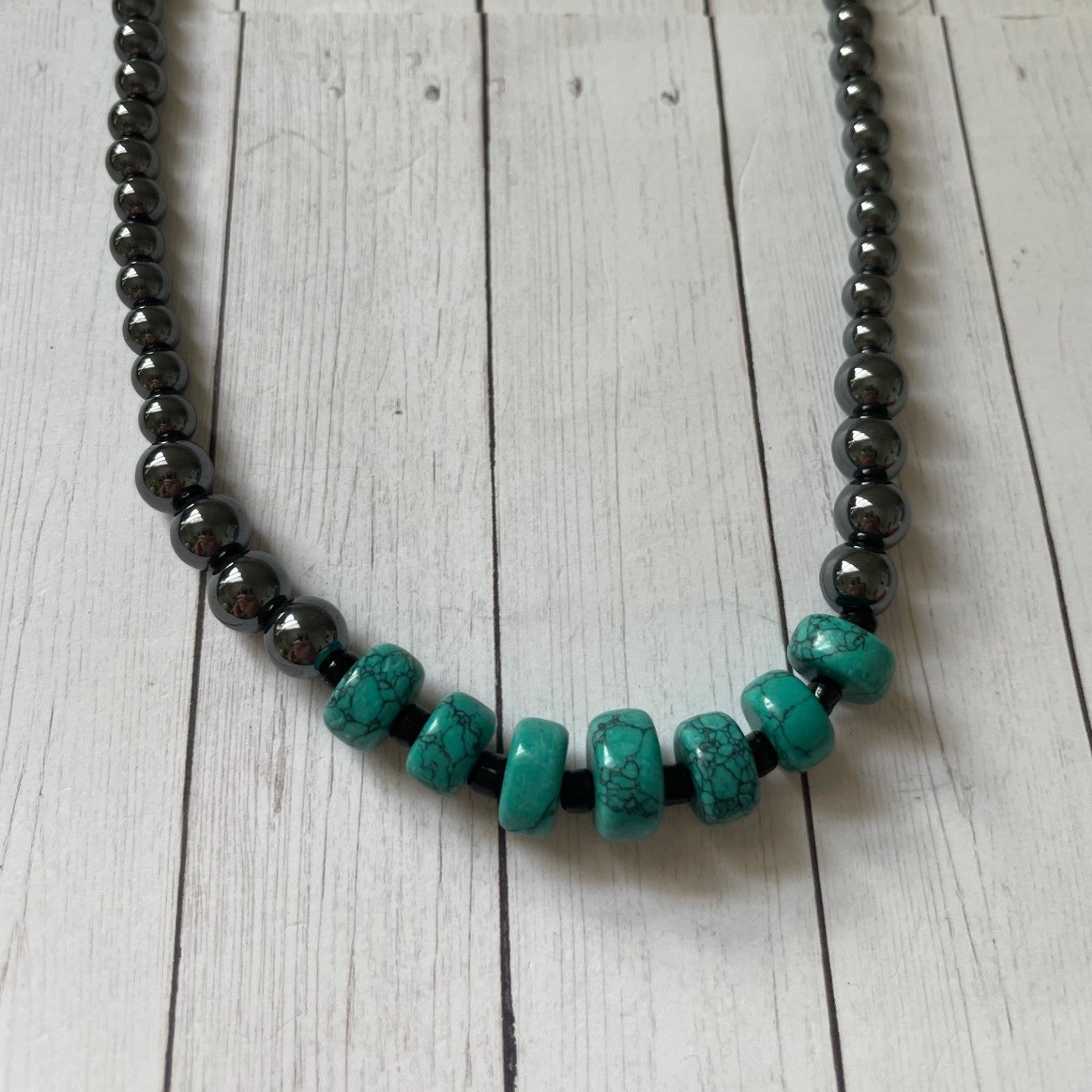 Necklace with alternating black and turquoise beads on a wooden surface