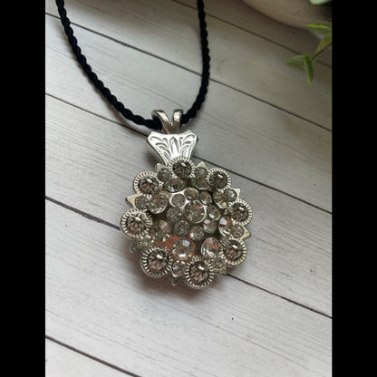 Silver concho western pendant necklace on a black cord against a light wooden background