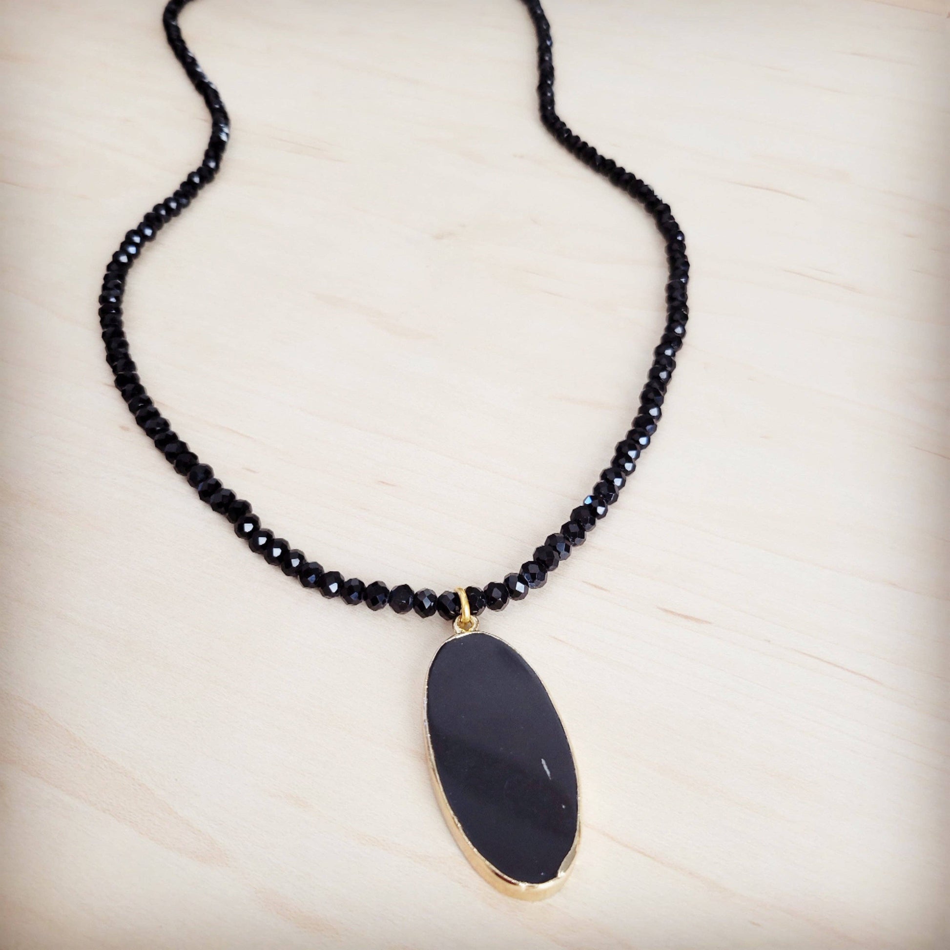 Necklace with black beaded chain and a large black pendant on a light wooden surface