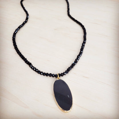 Necklace with black beaded chain and a large black pendant on a light wooden surface