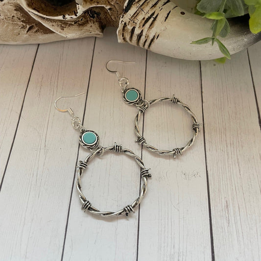 Silver hoop earrings with turquoise stones on a wooden surface with decorative shells and plants.