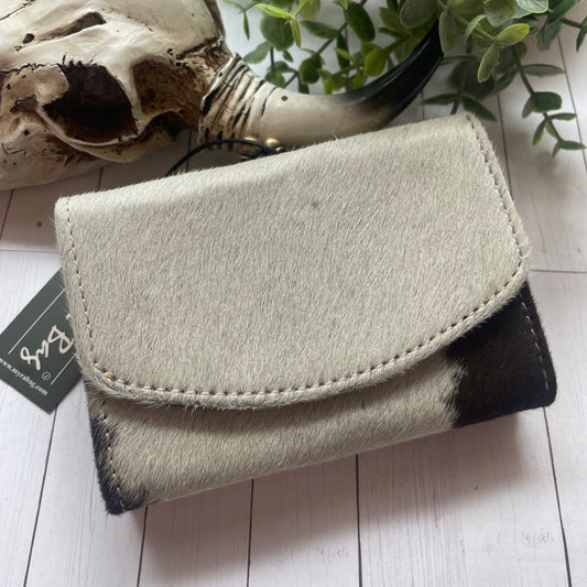 Black and white cowhide flap snap closure wallet on white wood with cowskull

