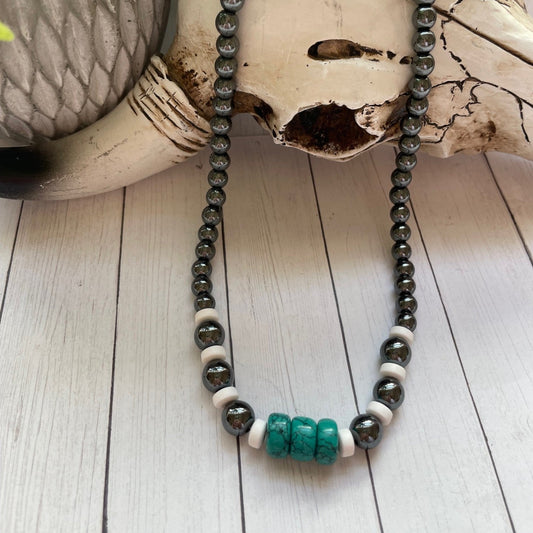 Beaded necklace with black, white, and turquoise beads on a wooden surface.