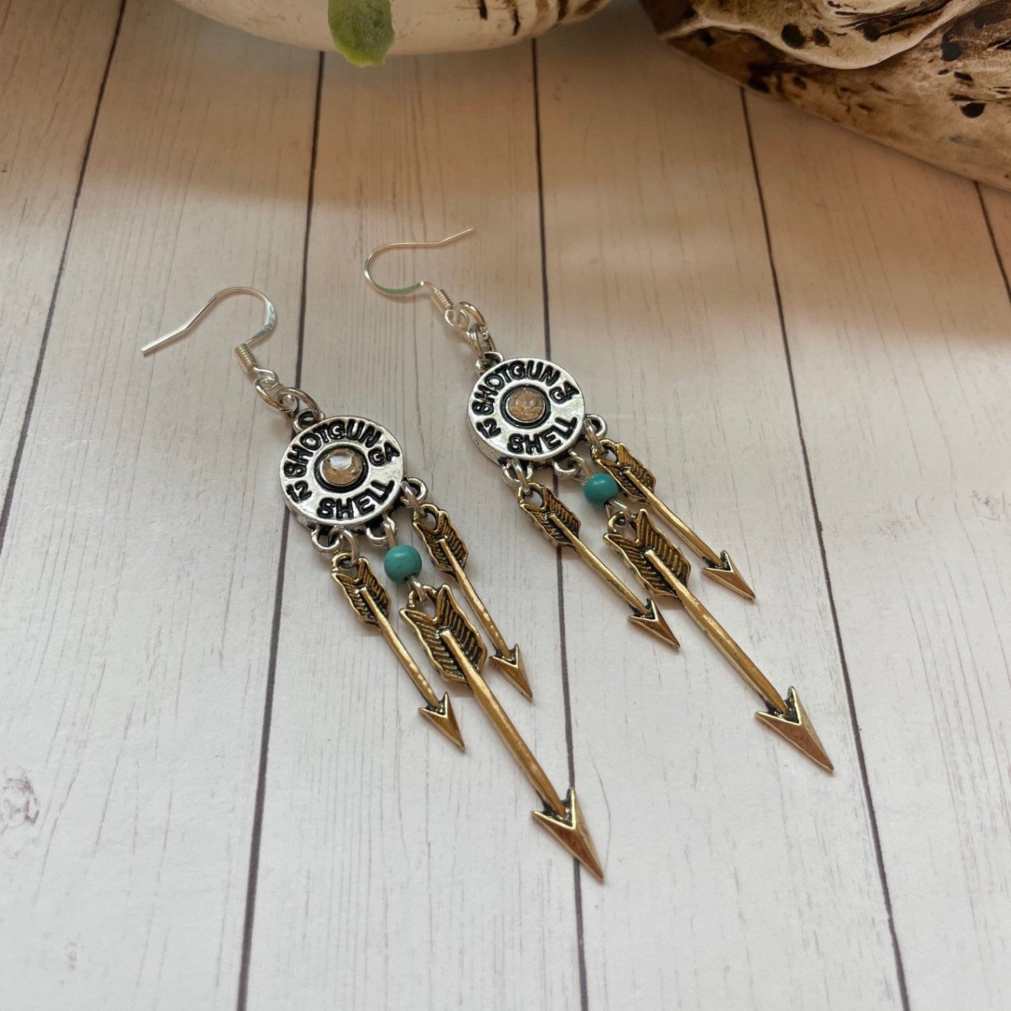 Pair of arrow-themed earrings on a wooden surface with a plant in the background