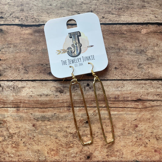 Gold rectangular long earrings on a wooden surface with a branded card underneath