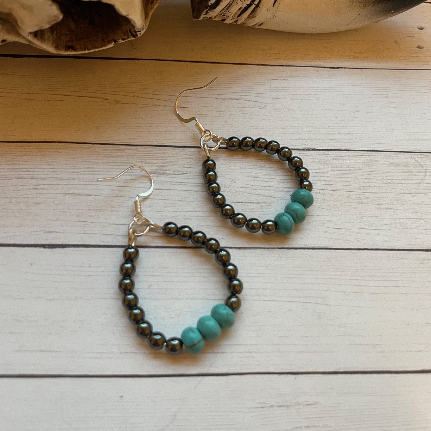 Pair of beaded earrings on a wooden surface with a large animal skull in the background.