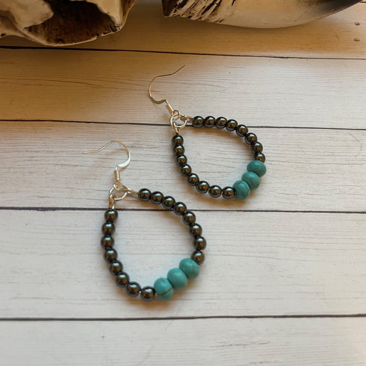Pair of beaded earrings on a wooden surface with a large animal skull in the background.