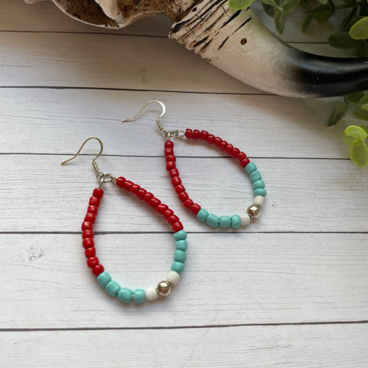 Beaded earrings on a wooden surface with a skull and plant in the background