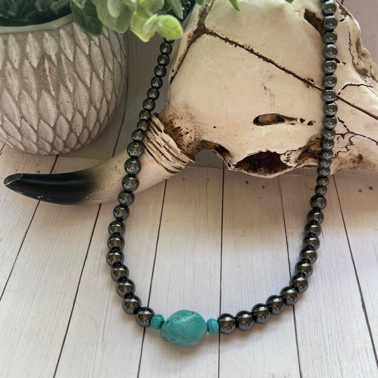 Necklace with a turquoise bead on a wooden surface with a plant in the background