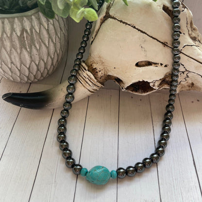 Necklace with a turquoise bead on a wooden surface with a plant in the background