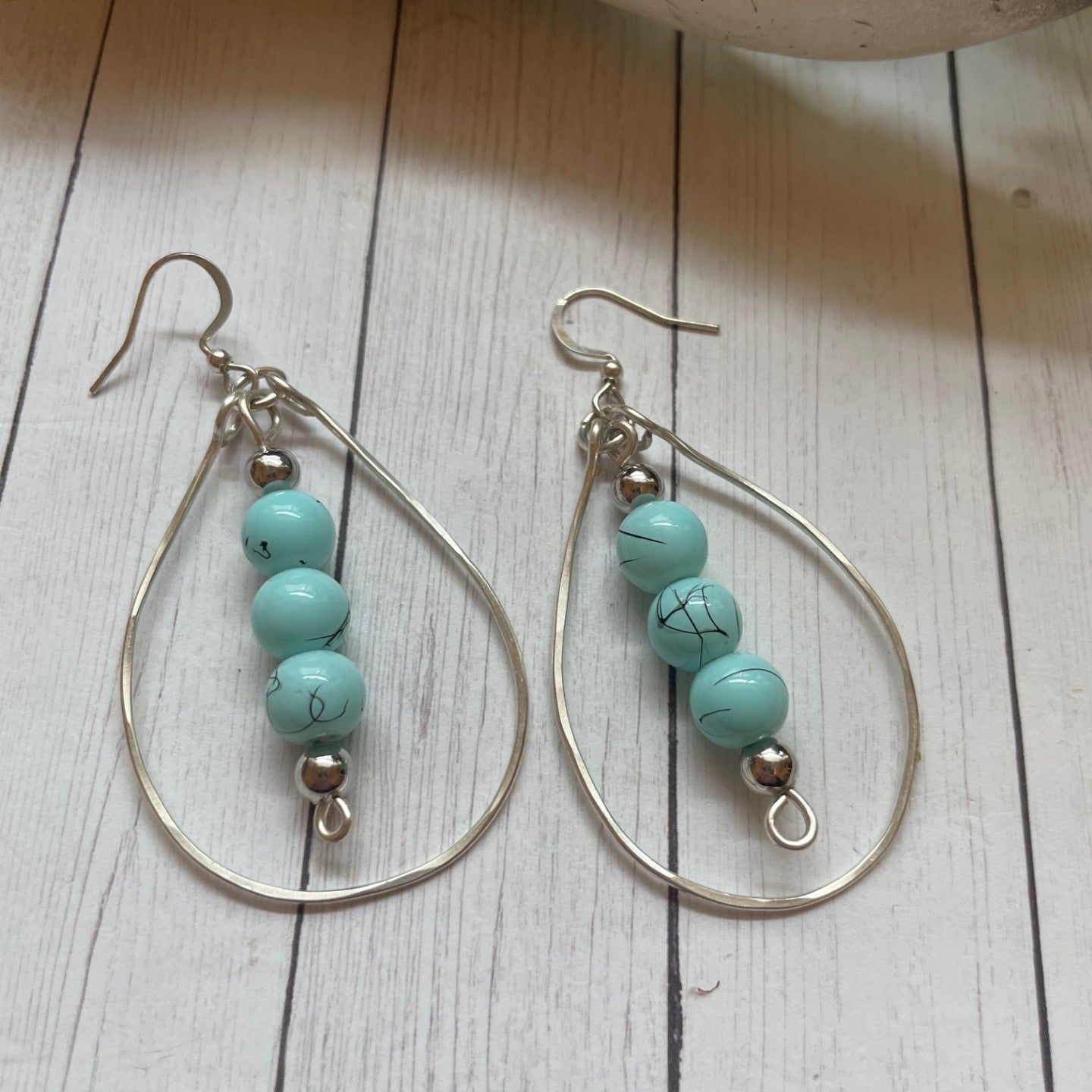 Three Turquoise beads inside a silver teardrop shape earrings on a wooden surface