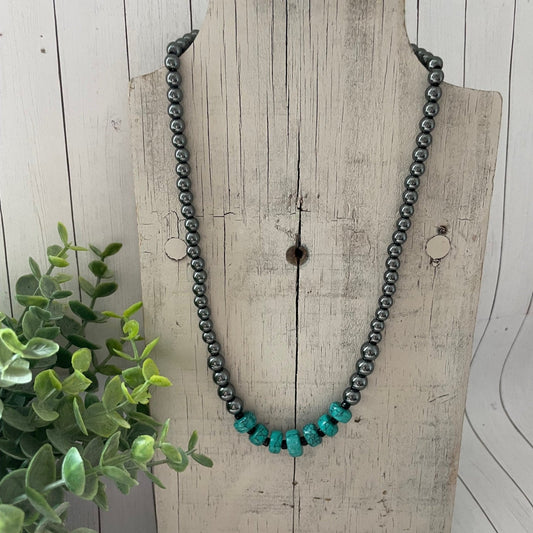 Necklace with black and turquoise beads on a wooden surface with a plant in the background