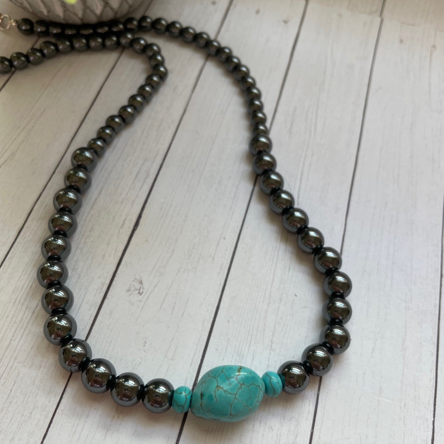 Necklace with black beads and a turquoise bead on a wooden surface