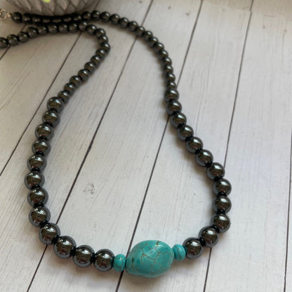 Necklace with black beads and a turquoise bead on a wooden surface