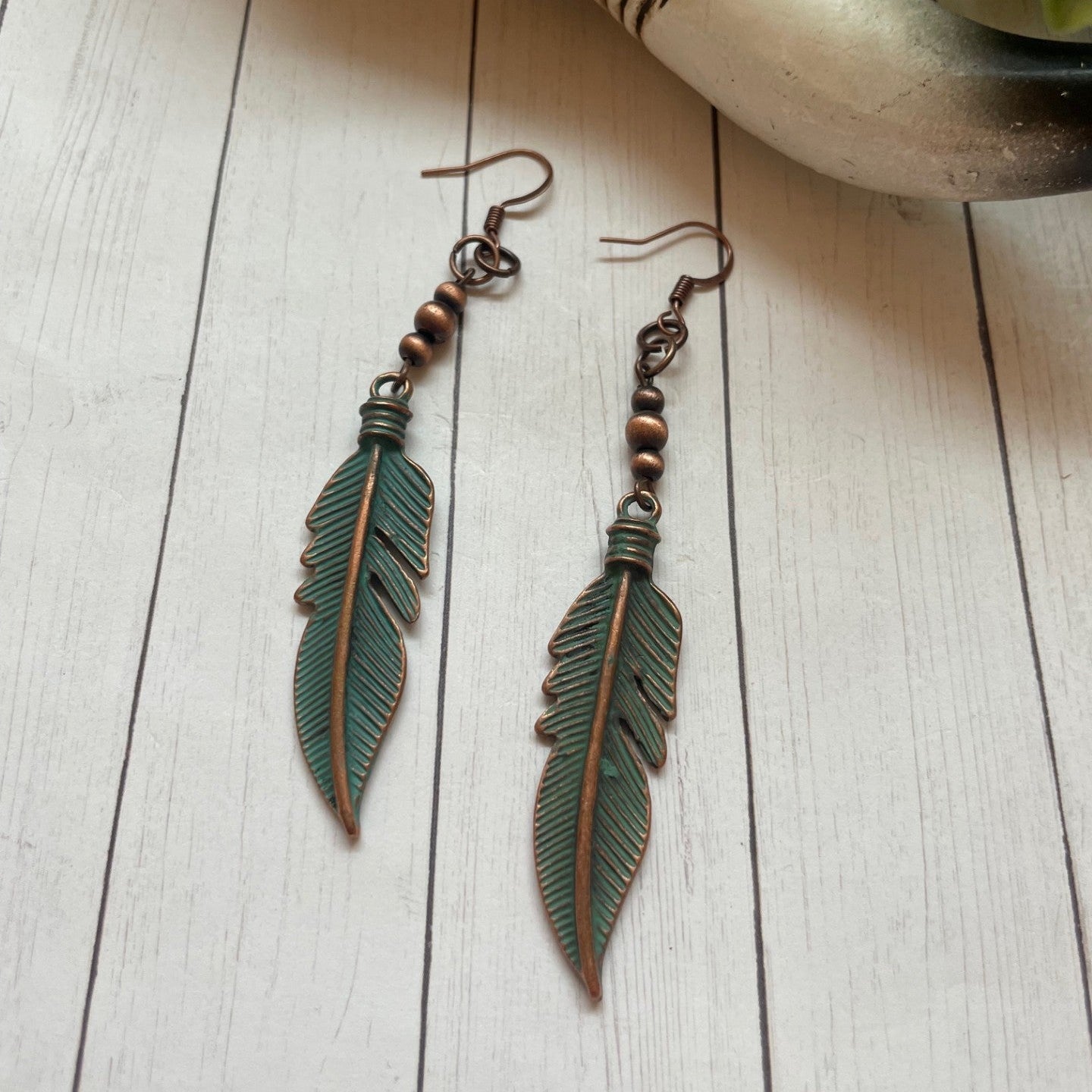 Feather-shaped earrings on a wooden surface with a plant in the background