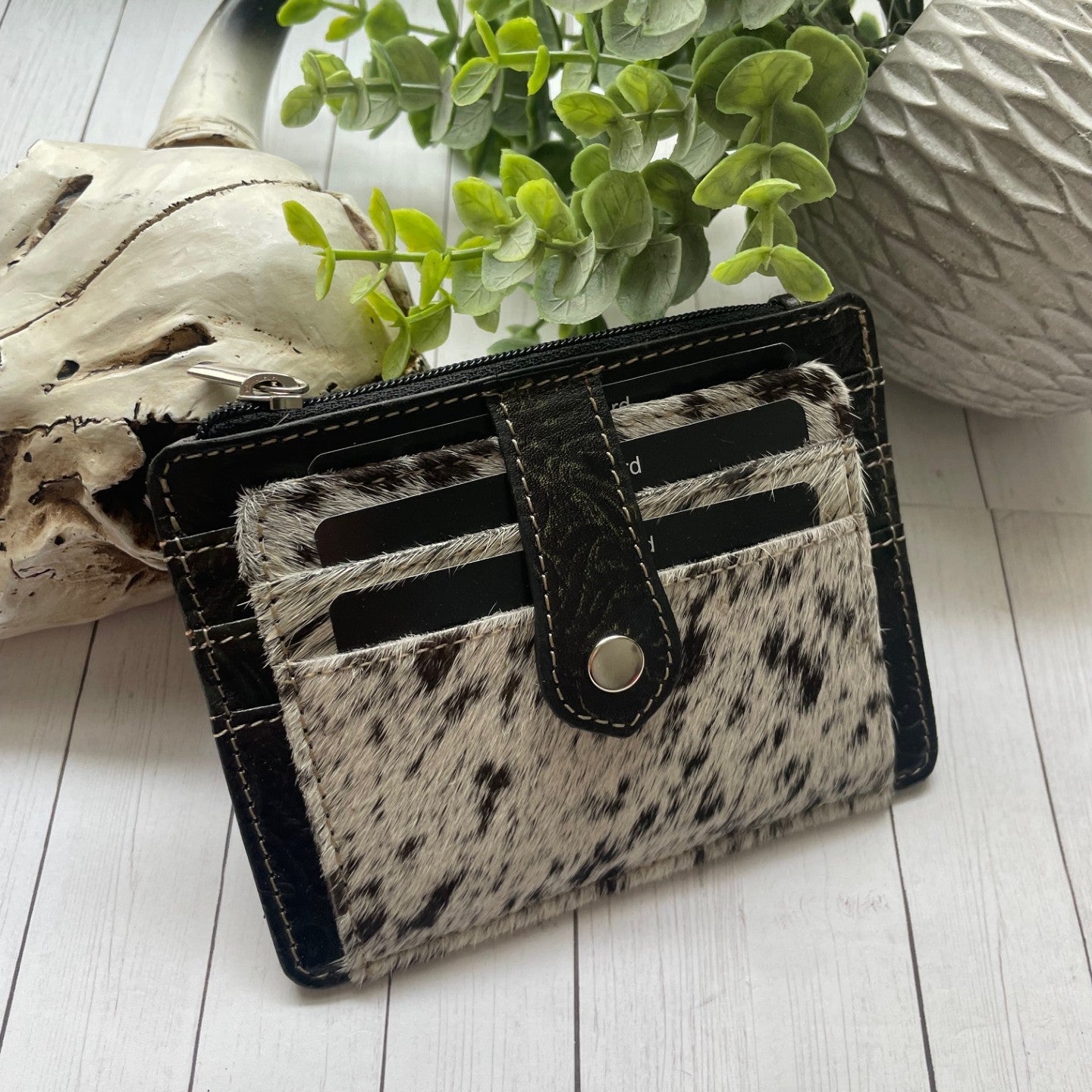 Black and white cowhide and leather wallet with a snap closure and credit card slots