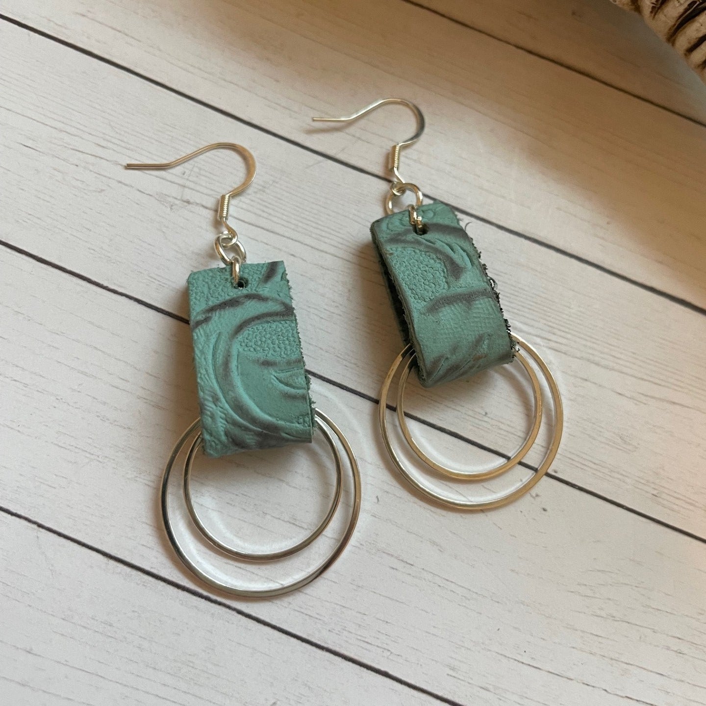 Pair of turquoise leather earrings with circular designs on a light wooden surface