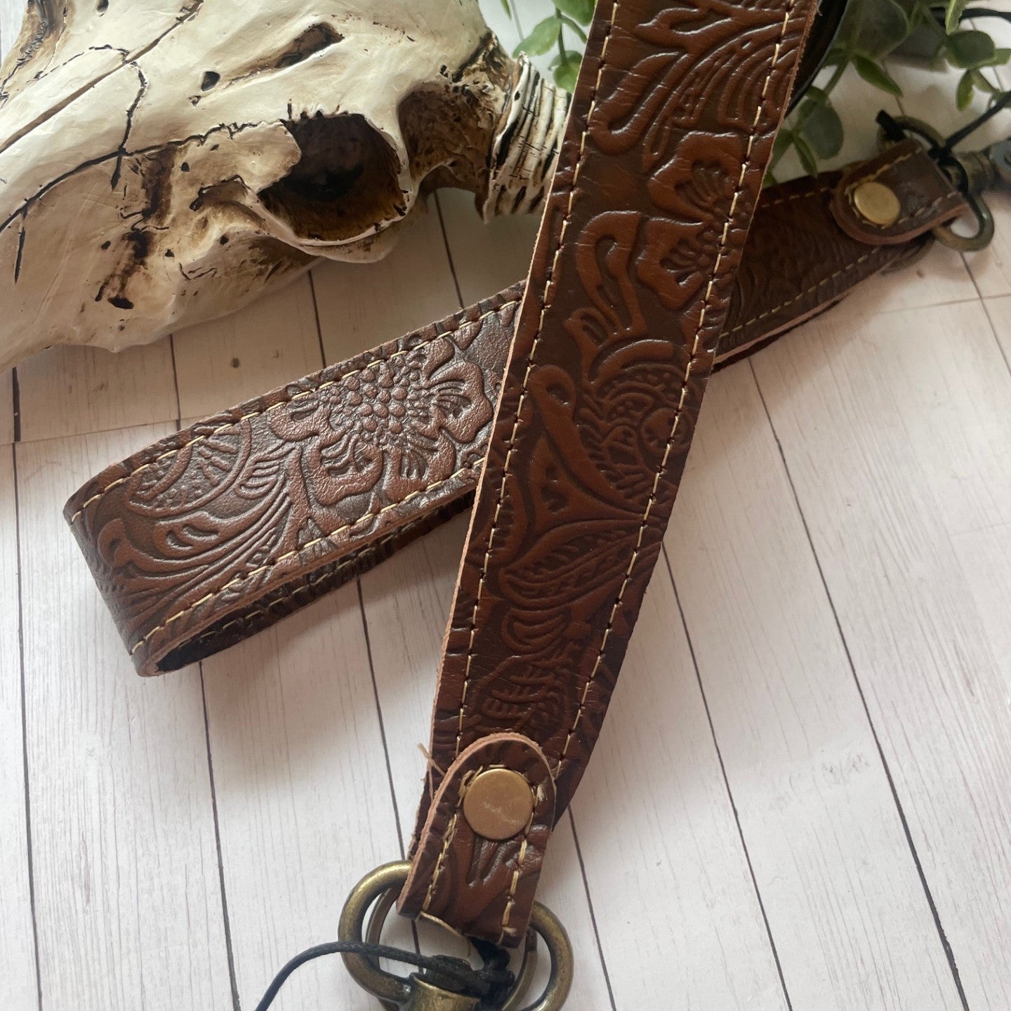 Brown leather strap with intricate patterns next to a cow skull on a wooden surface.