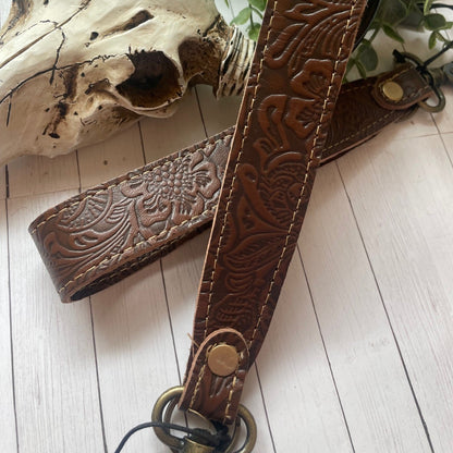 Brown leather strap with intricate patterns next to a cow skull on a wooden surface.