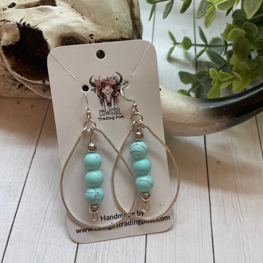 Three Turquoise beads inside a silver teardrop shape earrings on a wooden surface