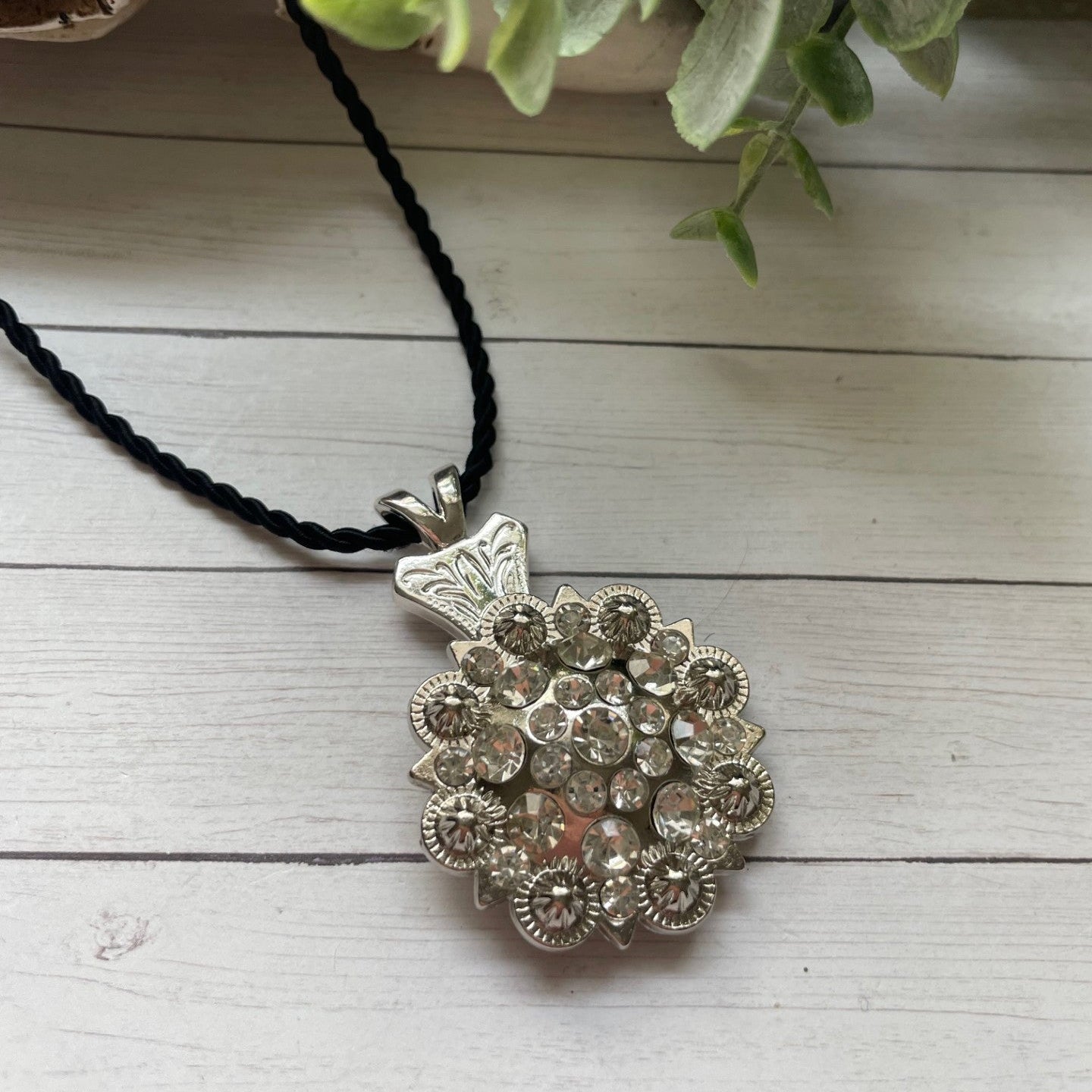 Silver floral pendant necklace on a black cord with a white wooden background
