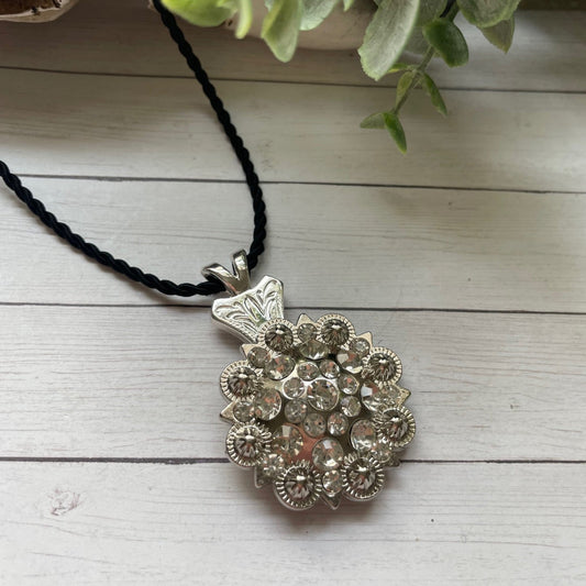 Silver floral pendant necklace on a black cord with a white wooden background