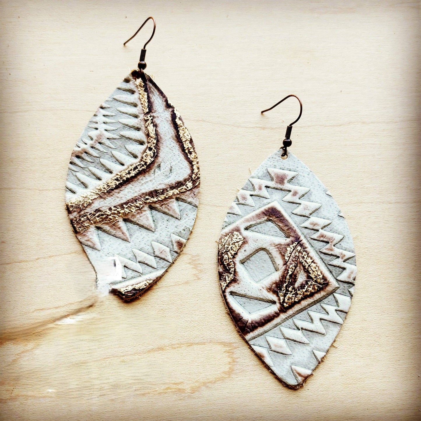 Pair of leather earrings with geometric patterns on a wooden surface