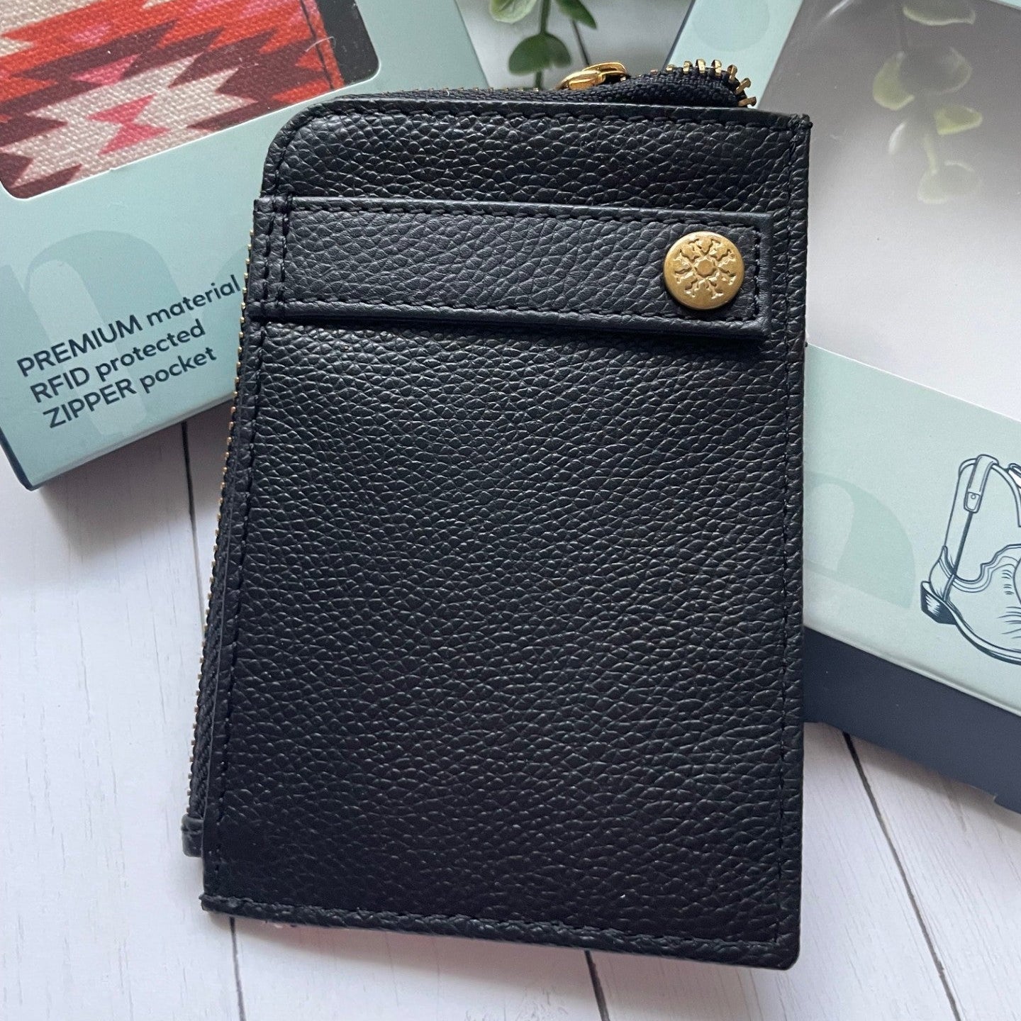 Black leather wallet with gold button on a white surface with books and a plant in the background