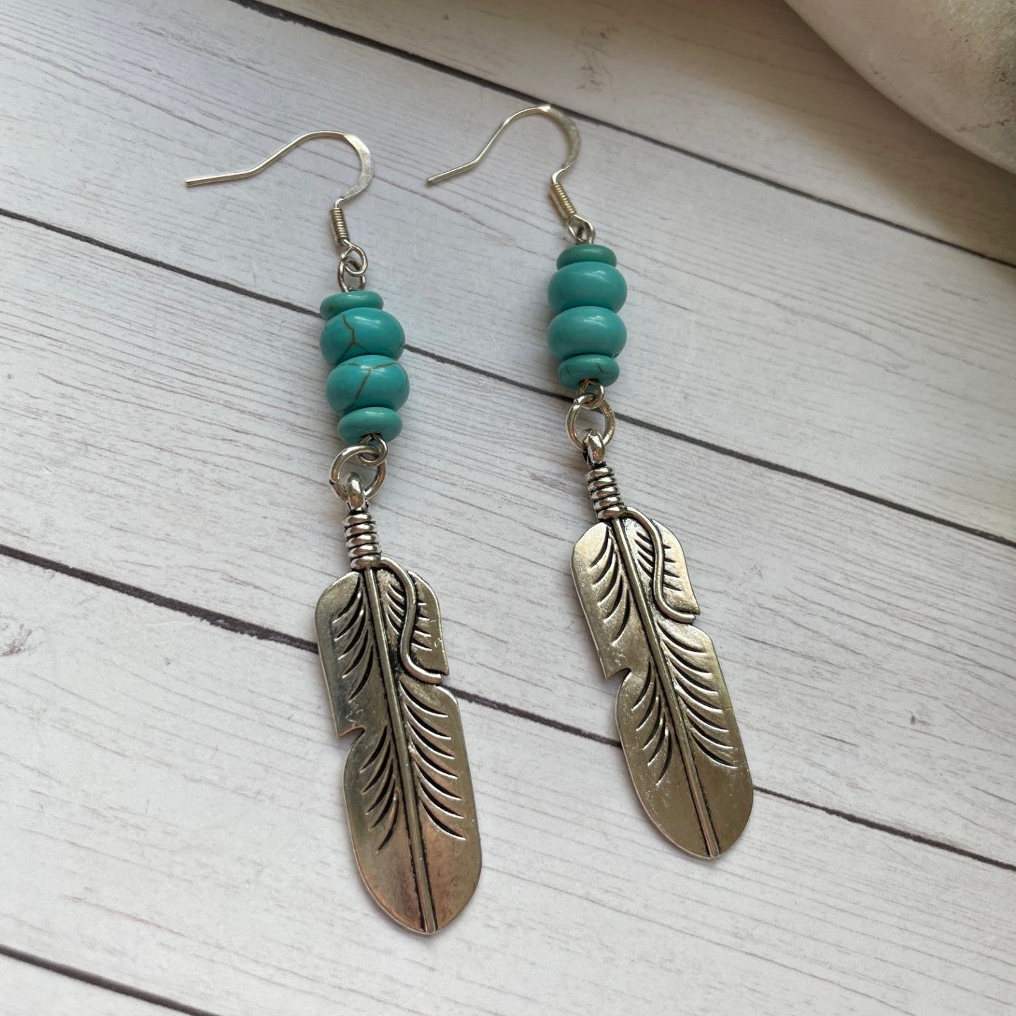Feather-shaped earrings with turquoise beads on a wooden surface