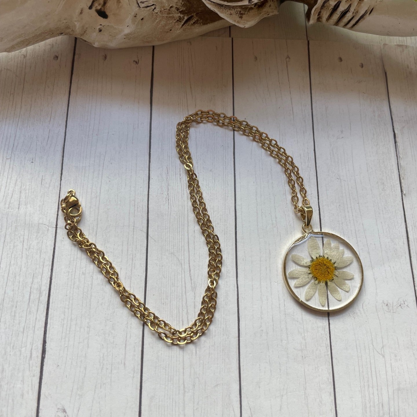 Gold necklace with a pendant featuring a pressed flower on a wooden surface