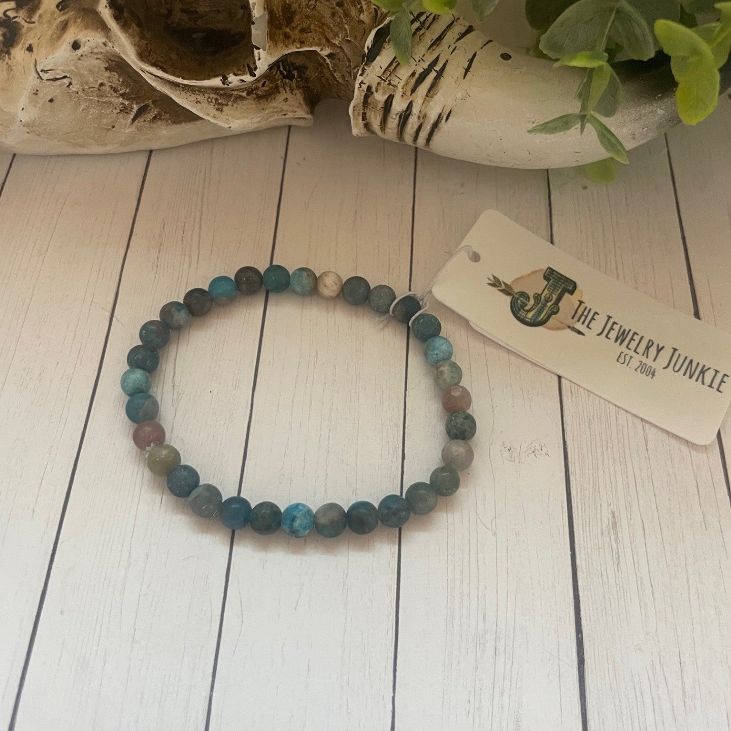Multicolored beaded bracelet on a white wooden surface with a skull and plant in the background.