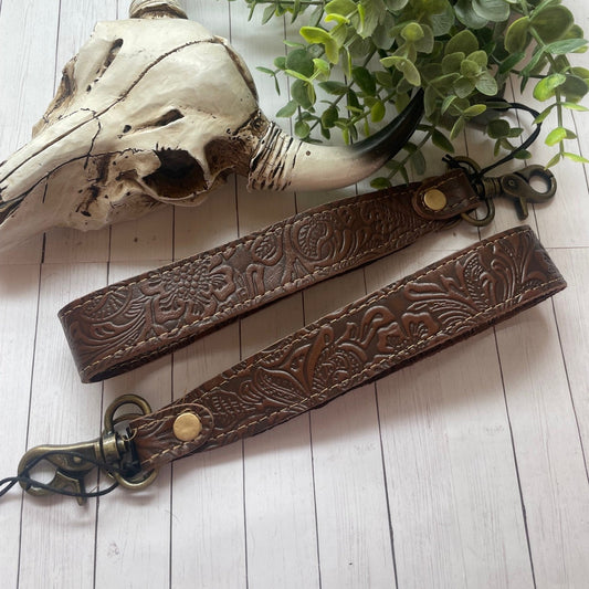 Brown leather strap with embossed design on a light wooden surface with a plant and skull.