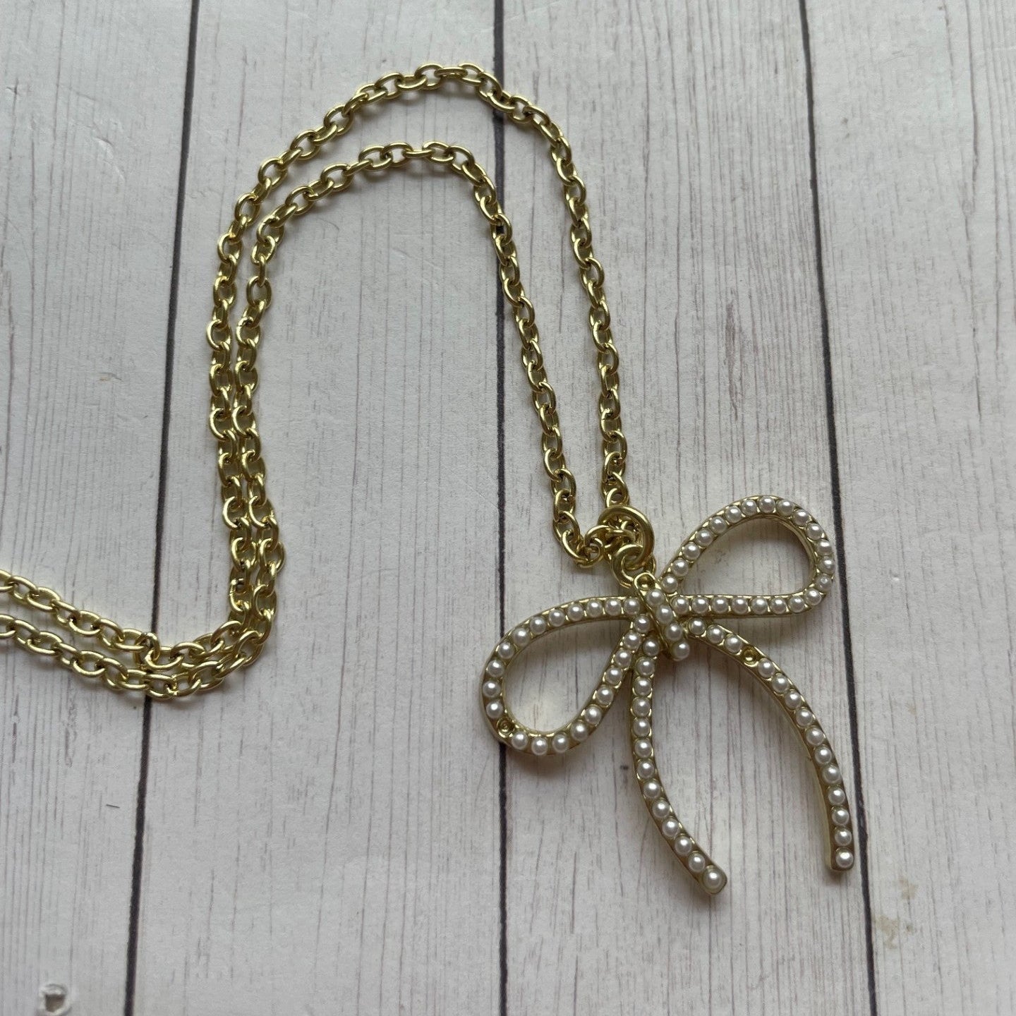 Gold chain necklace with a bow-shaped pendant on a wooden surface