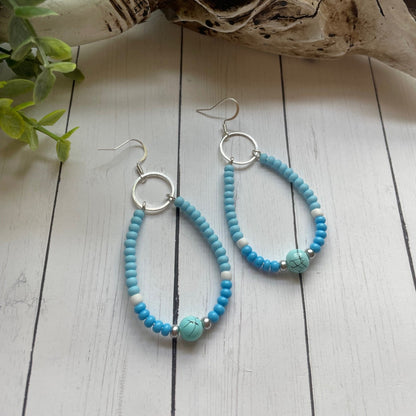 Turquoise beaded earrings on a white wooden surface with a skull and plant in the background