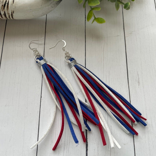 Pair of earrings with red, white, and blue tassels on a wooden surface.