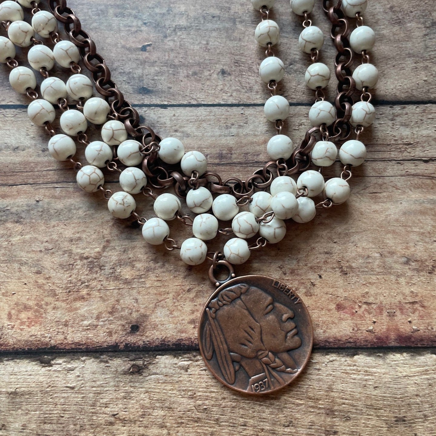 Necklace with white beads and a bronze pendant on a wooden surface