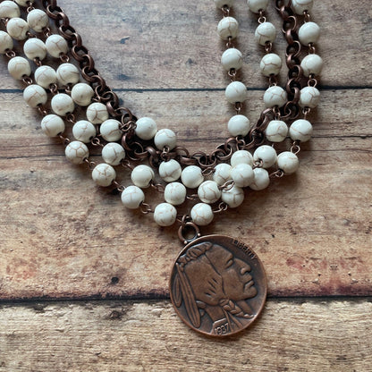 Necklace with white beads and a bronze pendant on a wooden surface