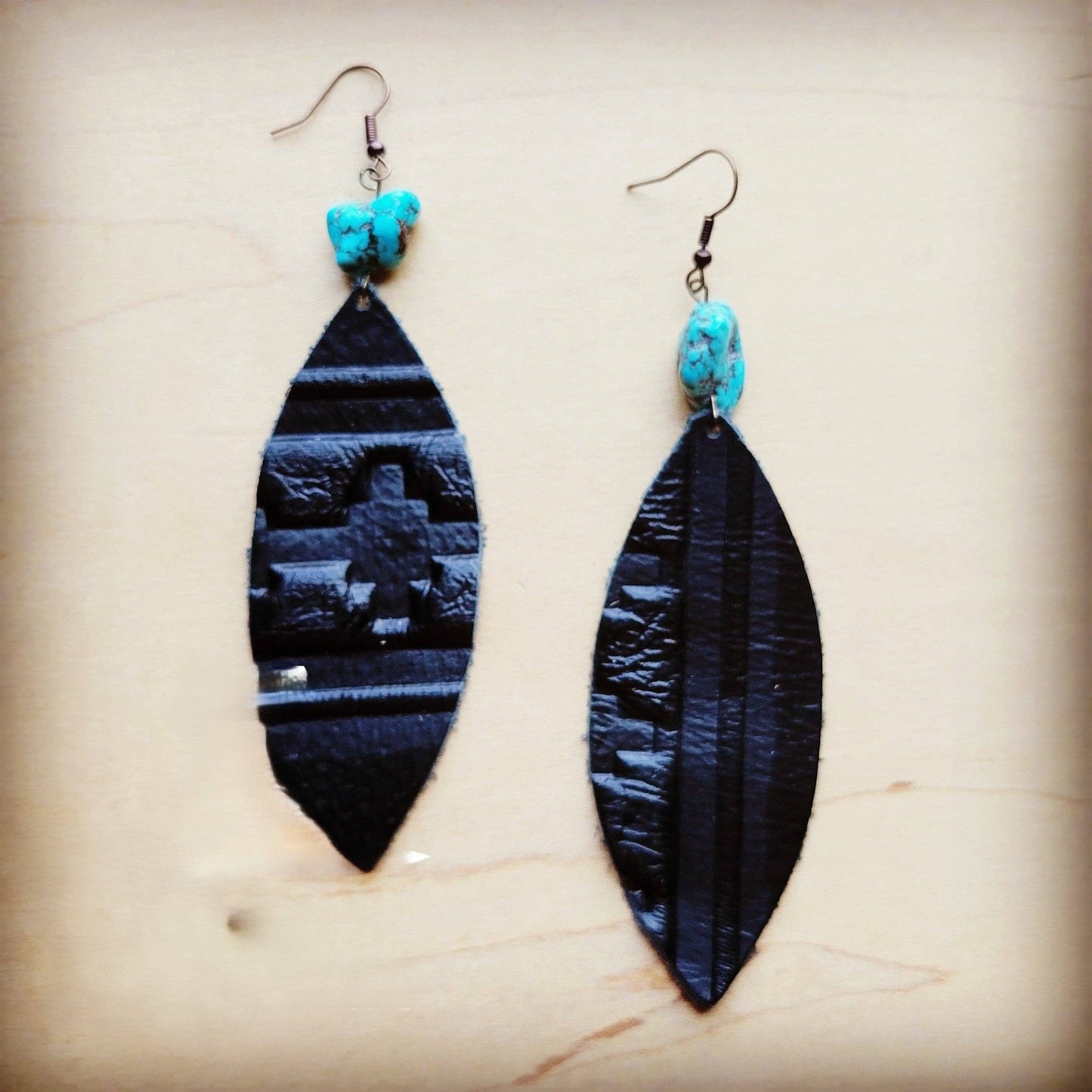 Black feather-shaped earrings with turquoise beads on a beige background
