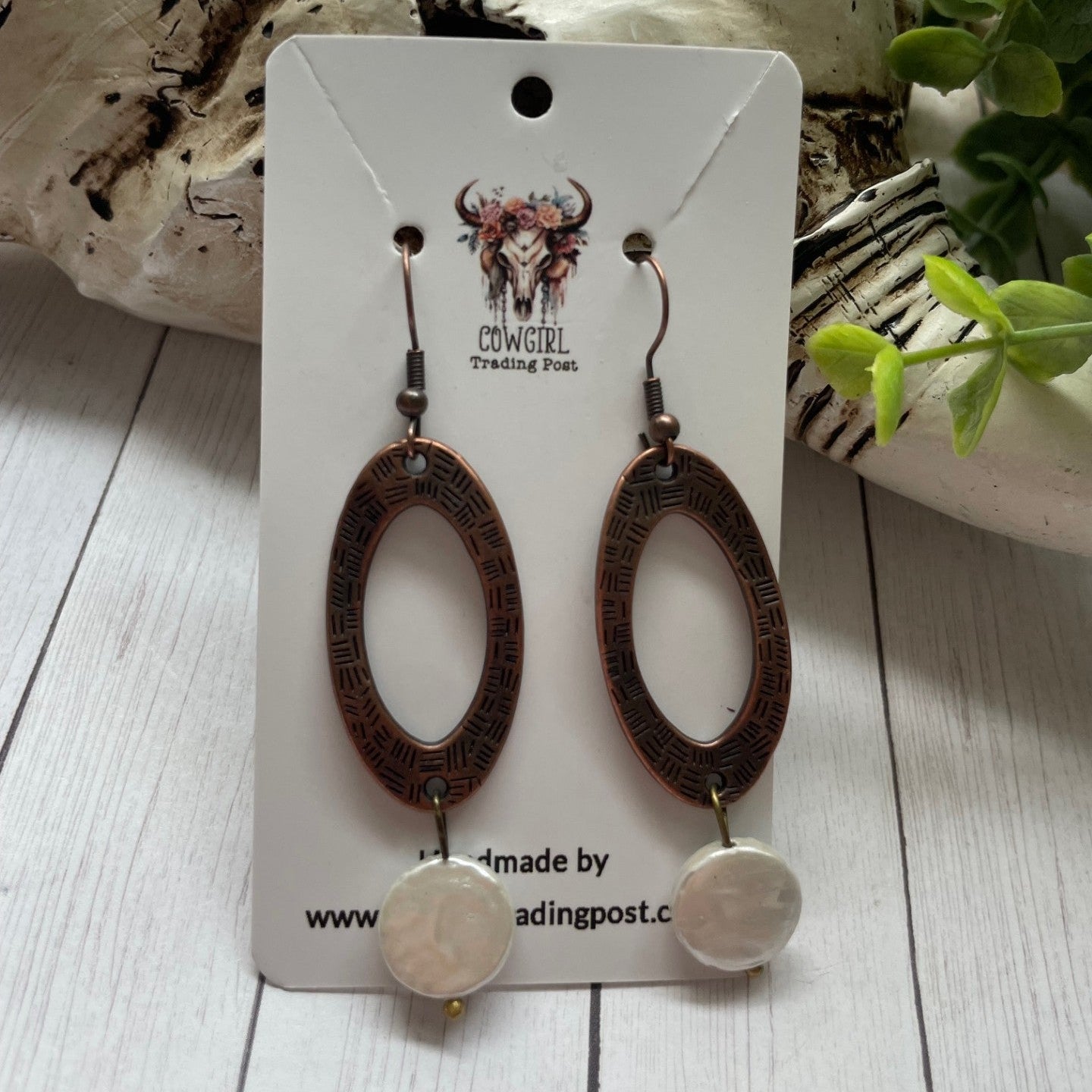 Pair of earrings on a card with 'Cowgirl Trading Post' branding, displayed on a wooden surface.