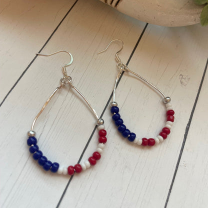 Pair of hoop earrings with red, white, and blue beads on a wooden surface.