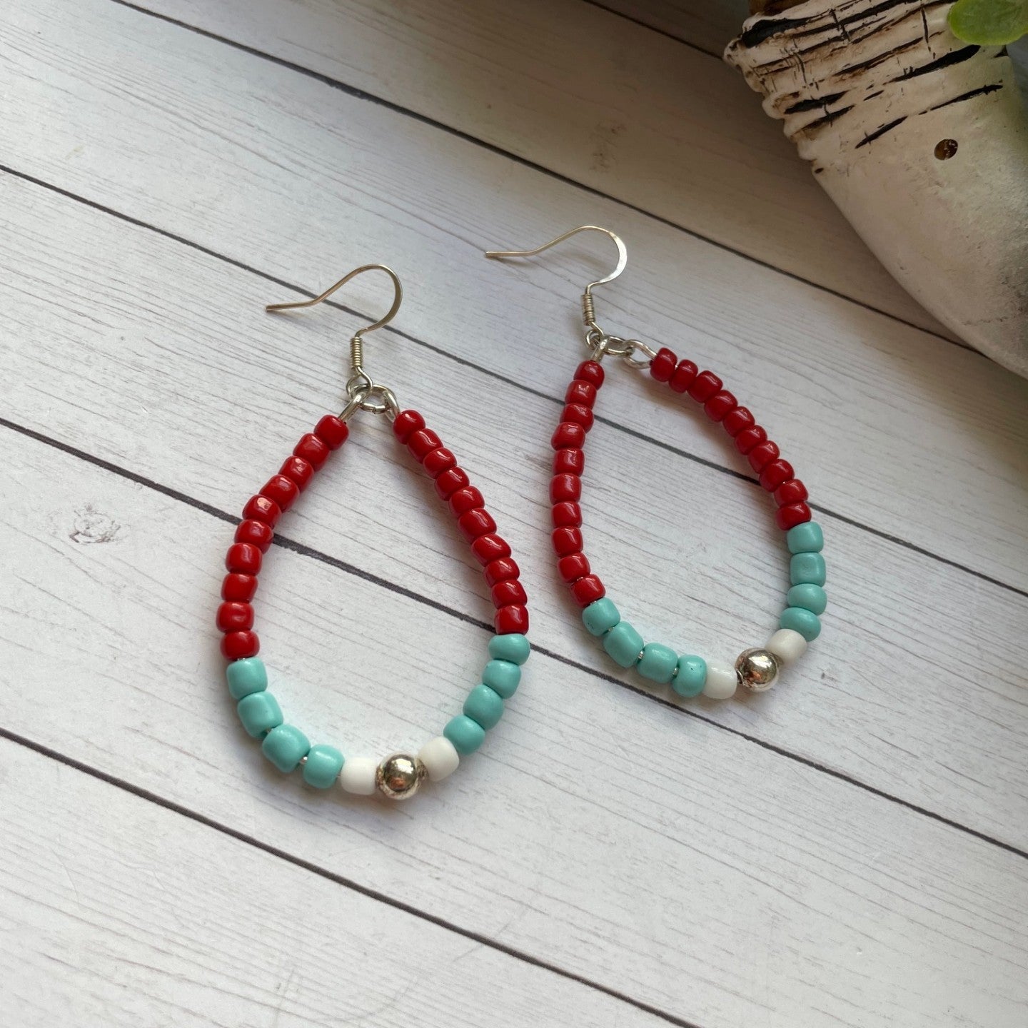 Beaded earrings with red, turquoise, and white beads on a wooden surface.
