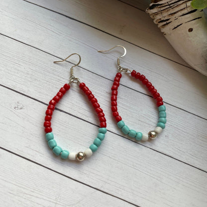 Beaded earrings with red, turquoise, and white beads on a wooden surface.
