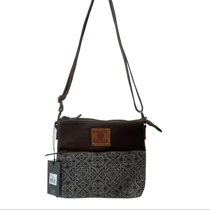 A dark brown and black crossbody bag with a patterned lower half, a brown leather patch on the front, and a black hangtag, shown against a plain white background.