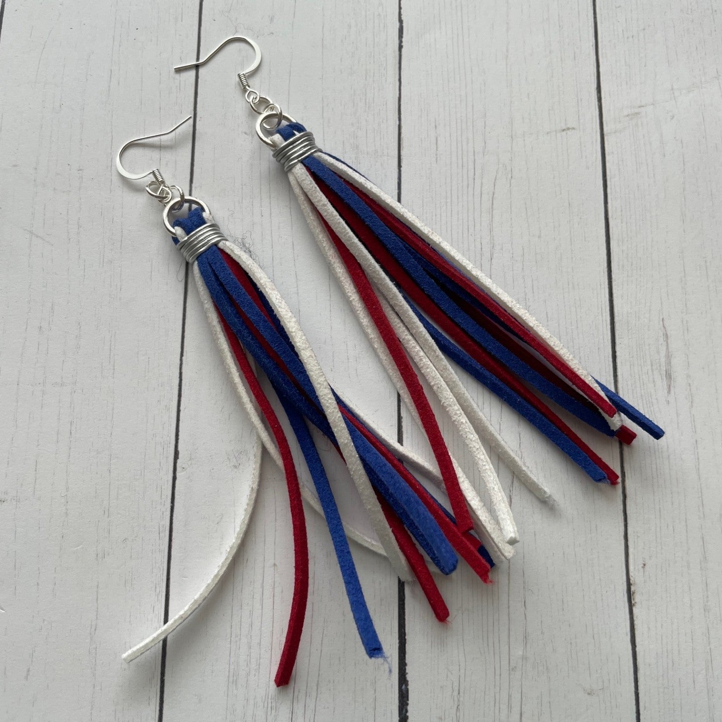 Tassel earrings with red, blue, and white ribbons on a light wooden surface