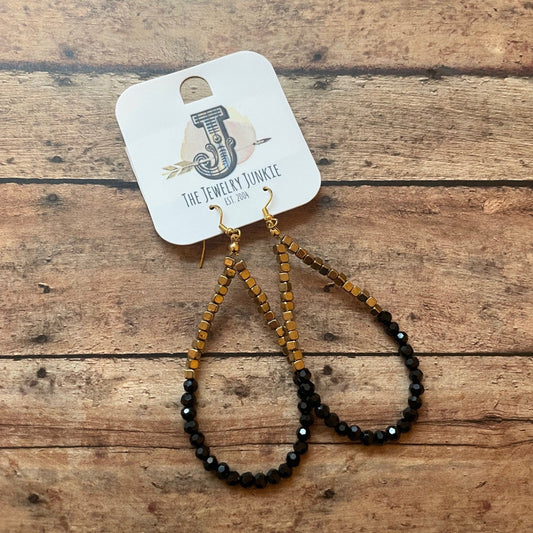 Pair of beaded earrings on a wooden surface with a branded card.