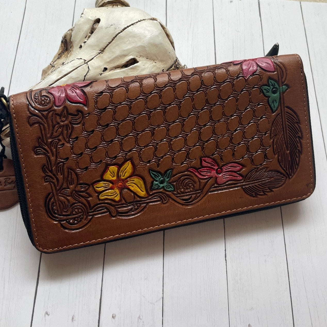 Brown leather wallet with floral designs on a white wooden surface