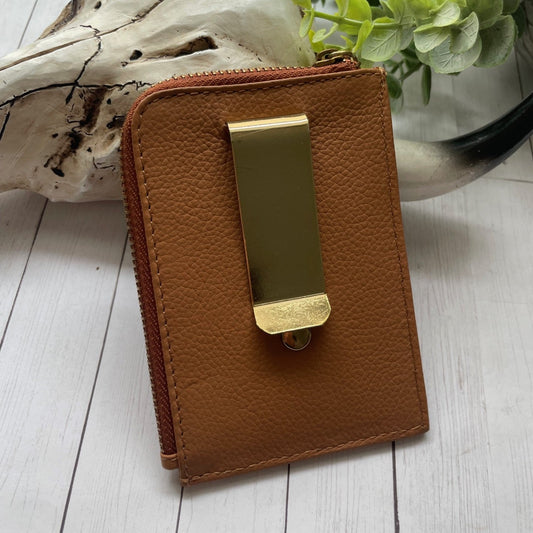 Brown leather wallet with gold clip on a white wooden surface with a plant in the background