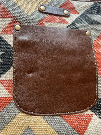 Brown leather pouch with button closures on a geometric patterned fabric background