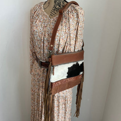 Mannequin wearing a floral dress with a brown leather belt and cowhide pouch against a white wall.